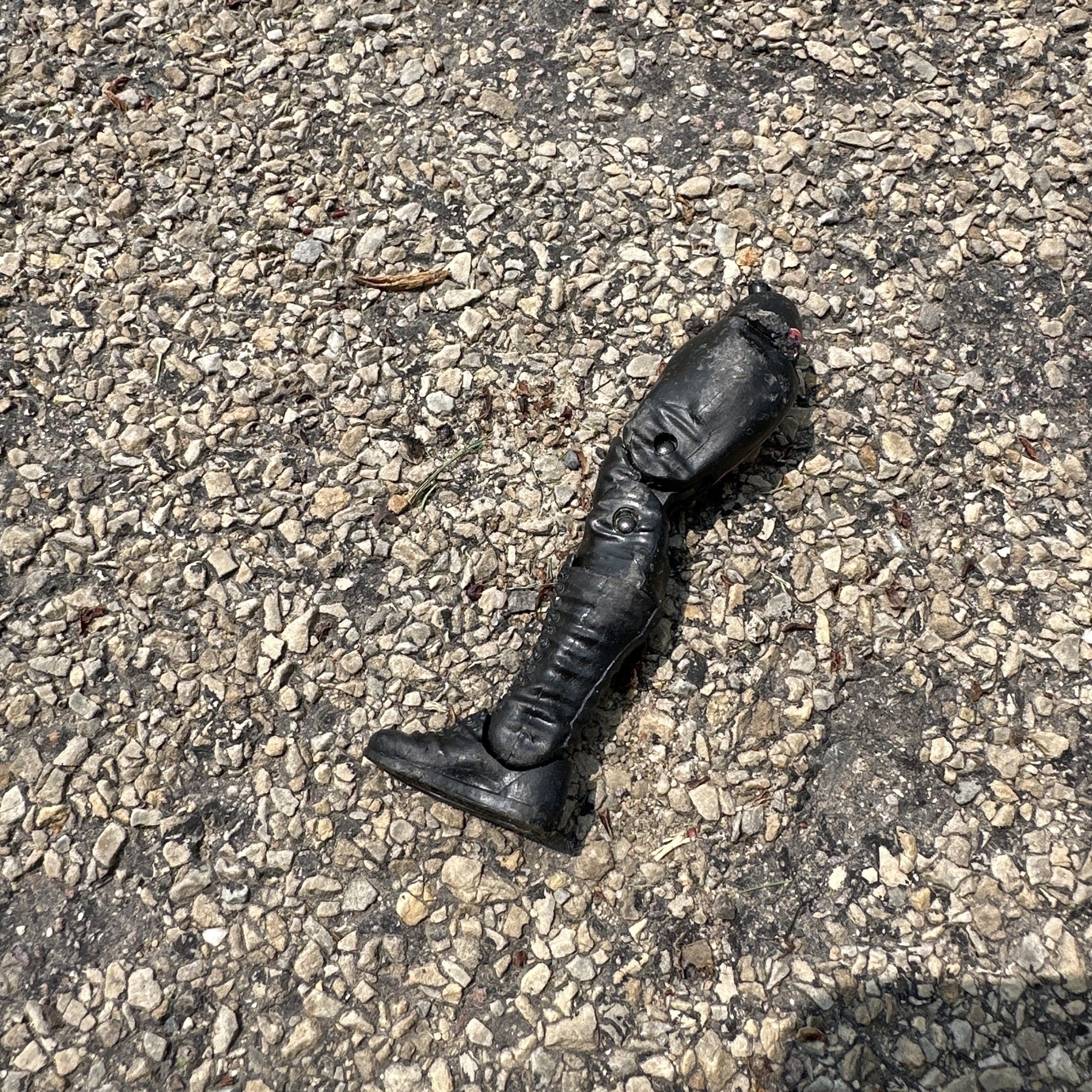 An action figure leg, detached from the action figure's body and sitting on the pavement of a street